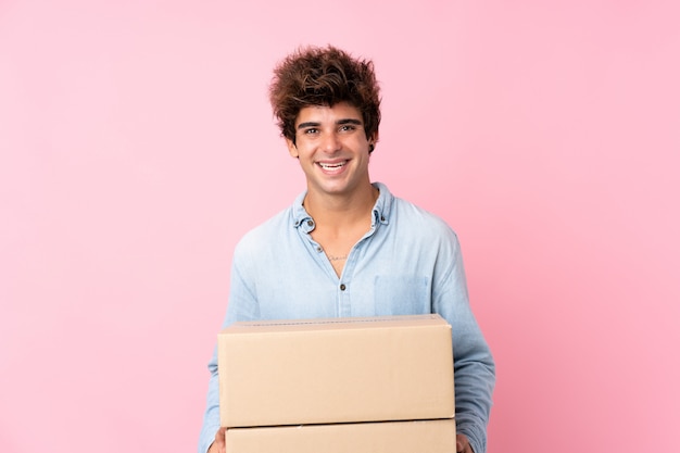 Young caucasian man over isolated pink wall holding a box to move it to another site