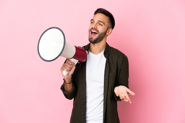 Young caucasian man isolated on pink wall holding a megaphone and with surprise facial expression