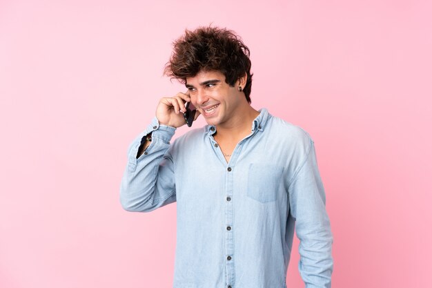 Young caucasian man over isolated pink wall keeping a conversation with the mobile phone with someone