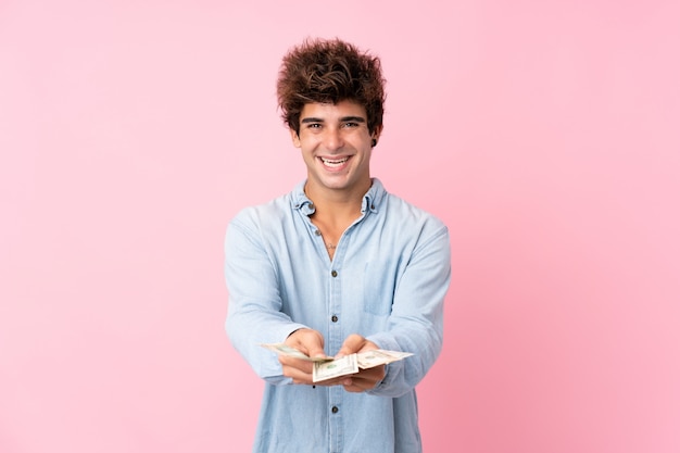 Young caucasian man over isolated pink wall taking a lot of money