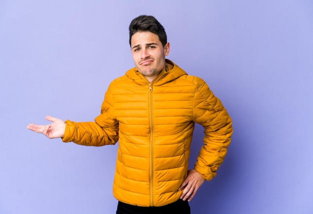 Young caucasian man isolated on purple background doubting and shrugging shoulders in questioning gesture.