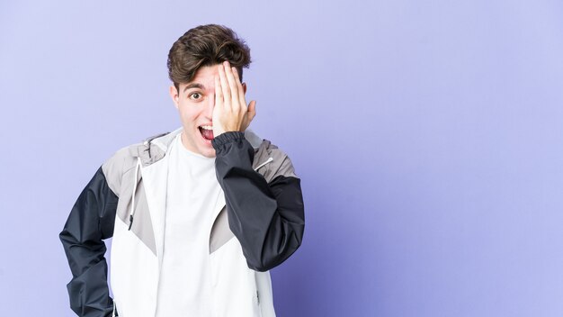 Young caucasian man isolated on purple background having fun covering half of face with palm