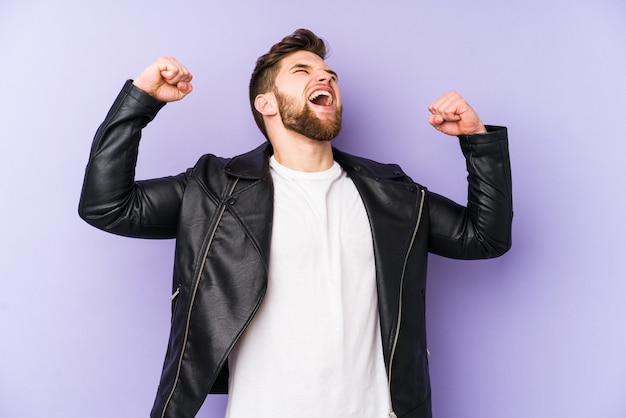 Young caucasian man isolated on purple background raising fist after a victory, winner concept