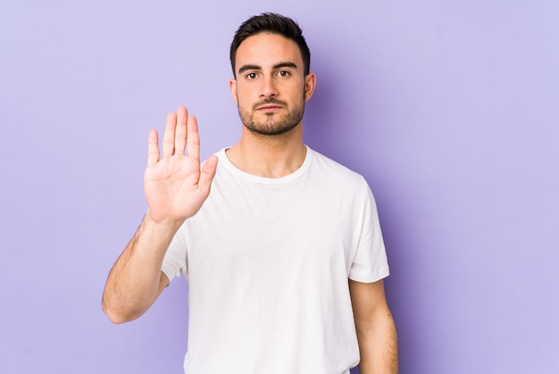 Young caucasian man isolated on purple background standing with outstretched hand showing stop sign, prevonting you.