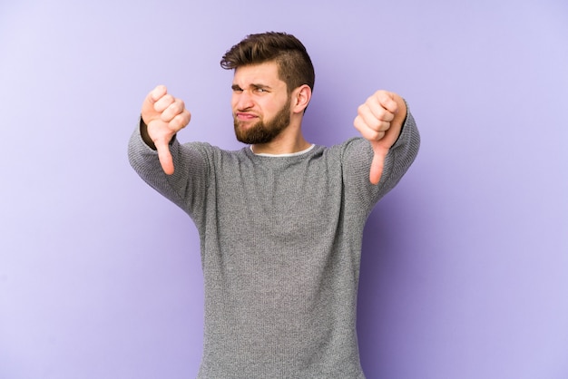 Young caucasian man isolated on purple showing thumb down, disappointment concept.