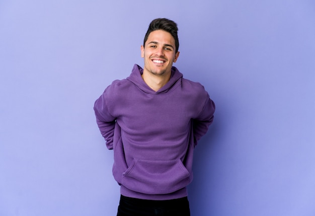 Young caucasian man isolated on purple space happy, smiling and cheerful.