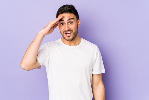 Young caucasian man isolated on purple space shouts loud, keeps eyes opened and hands tense.