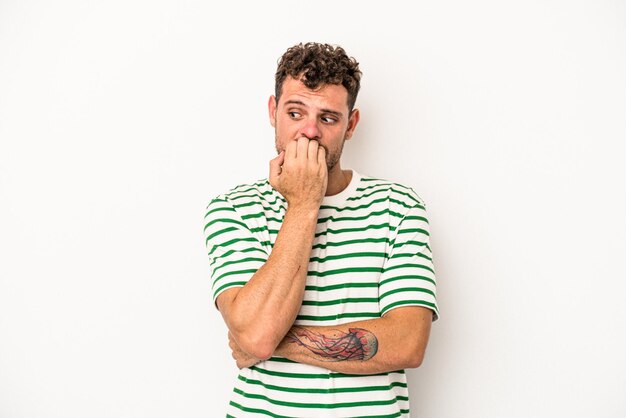 Young caucasian man isolated on white background biting fingernails, nervous and very anxious.