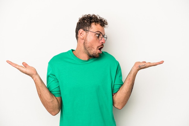 Young caucasian man isolated on white background confused and doubtful shrugging shoulders to hold a copy space.