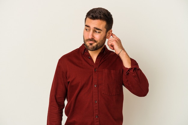 Young caucasian man isolated on white background covering ears with fingers, stressed and desperate by a loudly ambient.