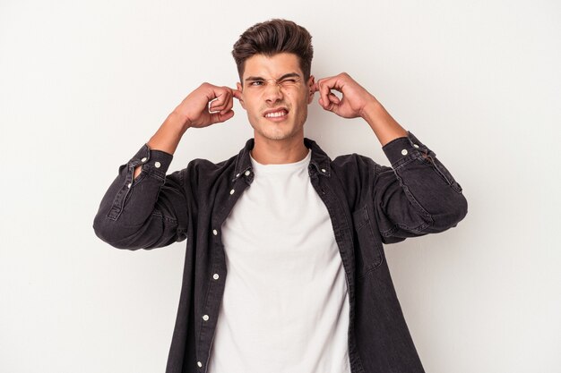 Young caucasian man isolated on white background covering ears with fingers, stressed and desperate by a loudly ambient.