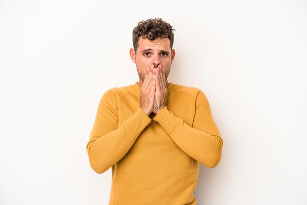 Young caucasian man isolated on white background covering mouth with hands looking worried.