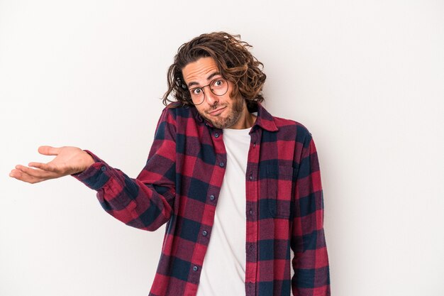 Young caucasian man isolated on white background doubting and shrugging shoulders in questioning gesture.