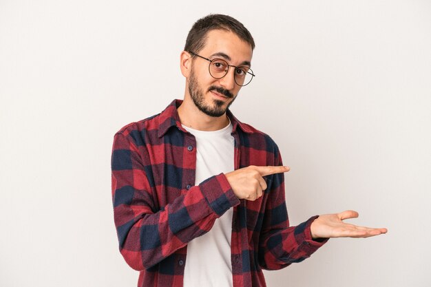 Young caucasian man isolated on white background excited holding a copy space on palm.