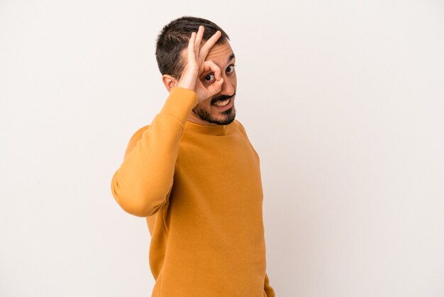 Foto giovane uomo caucasico isolato su sfondo bianco eccitato mantenendo il gesto ok sull'occhio.