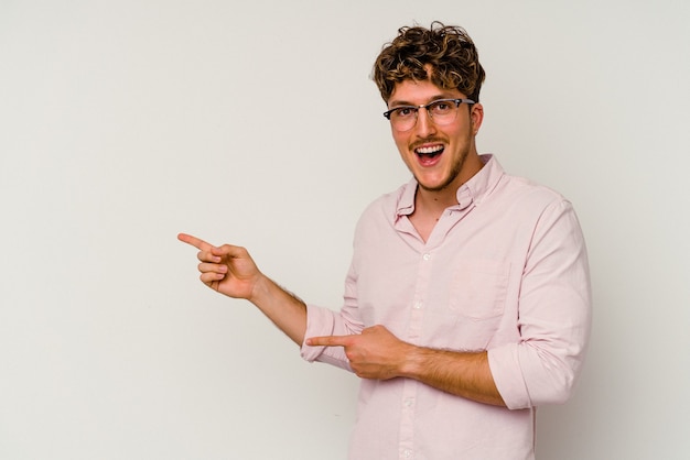 Young caucasian man isolated on white background excited pointing with forefingers away.