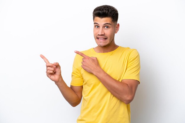 Young caucasian man isolated on white background frightened and pointing to the side