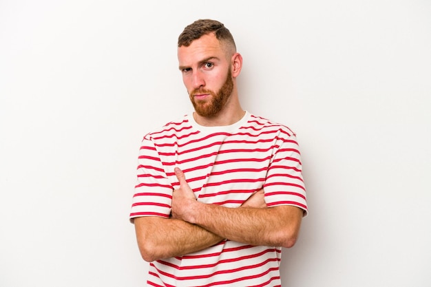 Young caucasian man isolated on white background frowning face in displeasure, keeps arms folded.