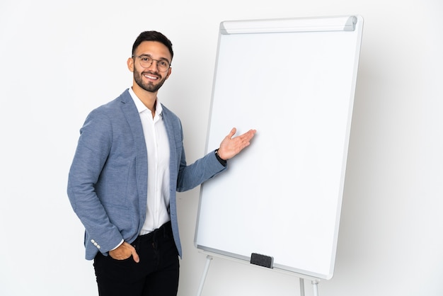 Young caucasian man isolated on white background giving a presentation on white board and pointing it
