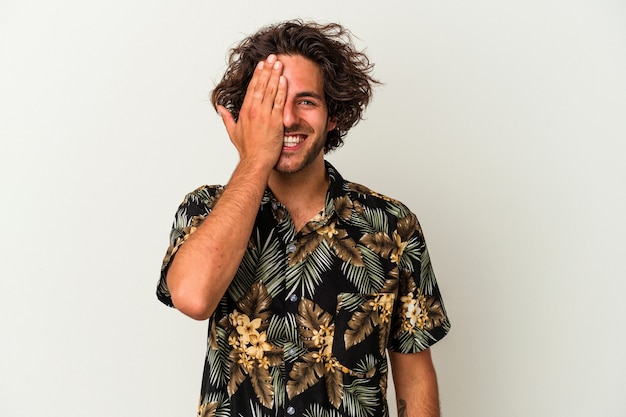 Young caucasian man isolated on white background having fun covering half of face with palm.