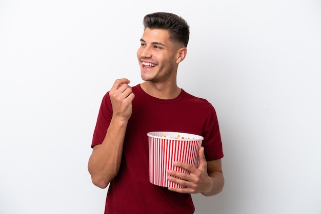 Young caucasian man isolated on white background holding a big bucket of popcorns
