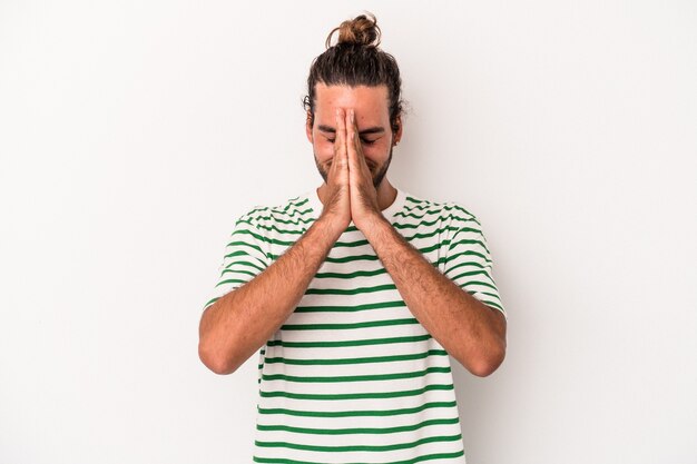 Young caucasian man isolated on white background holding hands in pray near mouth, feels confident.