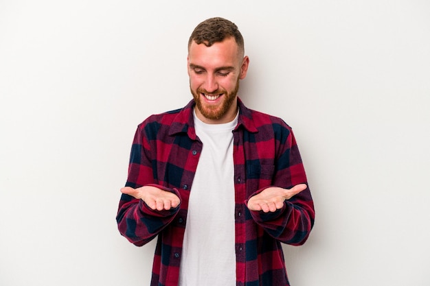 Young caucasian man isolated on white background holding something with palms, offering to camera.