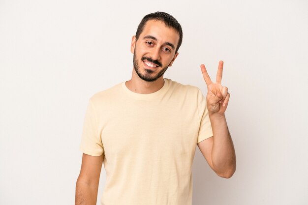 Young caucasian man isolated on white background joyful and carefree showing a peace symbol with fingers.