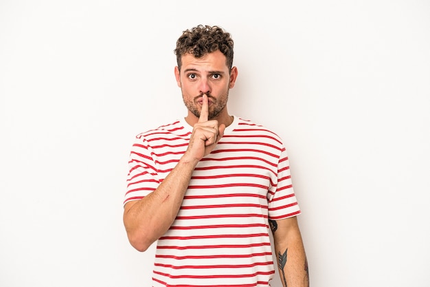 Young caucasian man isolated on white background keeping a secret or asking for silence.