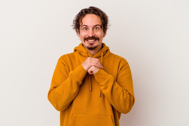 Young caucasian man isolated on white background keeps hands under chin, is looking happily aside.