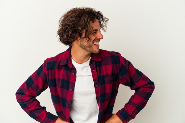 Young caucasian man isolated on white background laughs happily and has fun keeping hands on stomach.