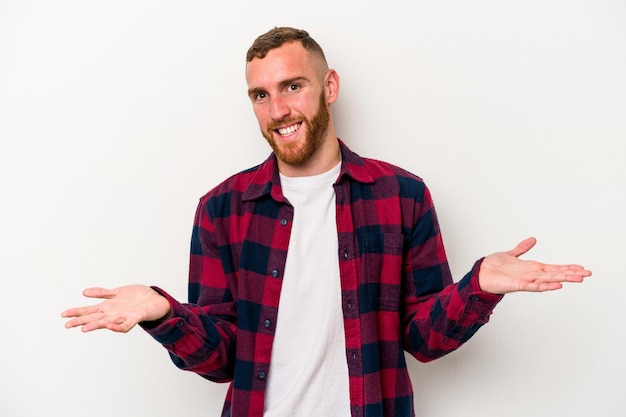 Young caucasian man isolated on white background makes scale with arms, feels happy and confident.