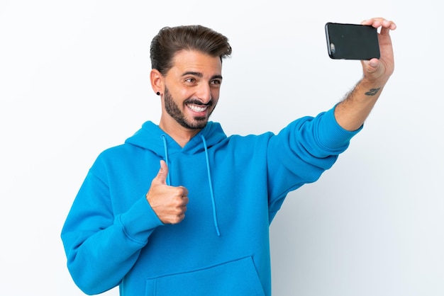 Young caucasian man isolated on white background making a selfie with mobile phone