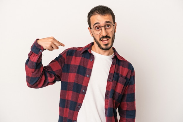 Young caucasian man isolated on white background person pointing by hand to a shirt copy space, proud and confident