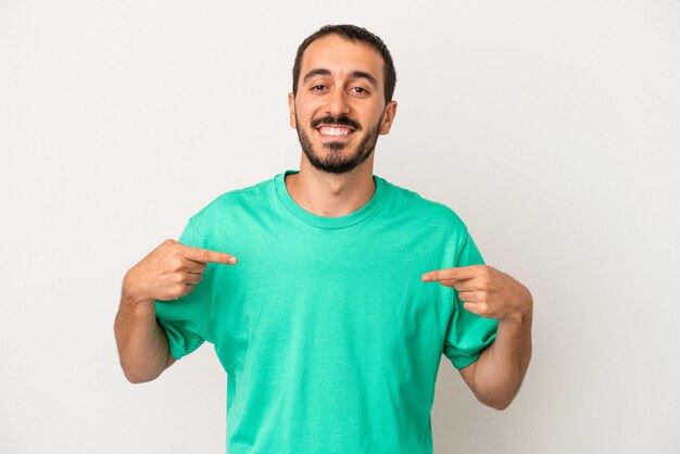 Young caucasian man isolated on white background person pointing by hand to a shirt copy space proud and confident