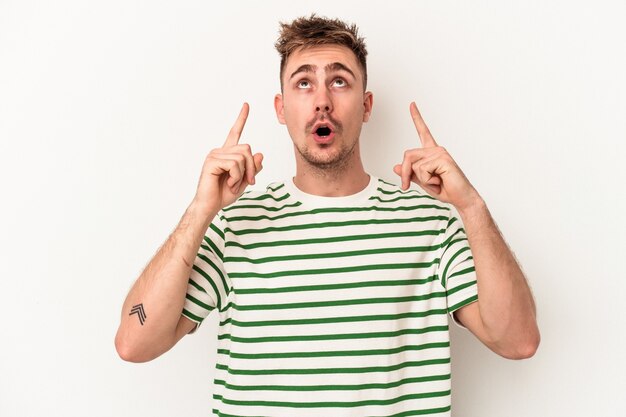 Young caucasian man isolated on white background pointing upside with opened mouth.