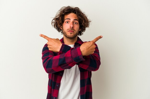 Young caucasian man isolated on white background points sideways, is trying to choose between two options.