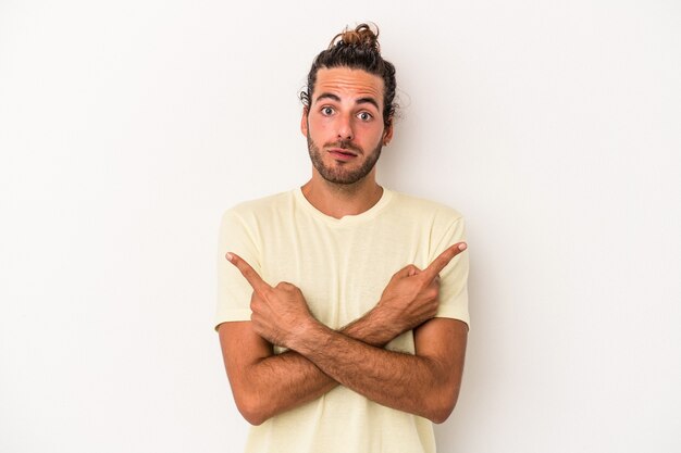 Young caucasian man isolated on white background points sideways, is trying to choose between two options.
