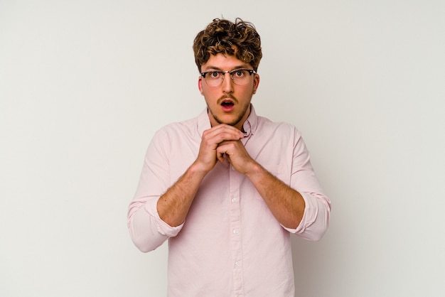 Young caucasian man isolated on white background praying for luck, amazed and opening mouth looking to front.