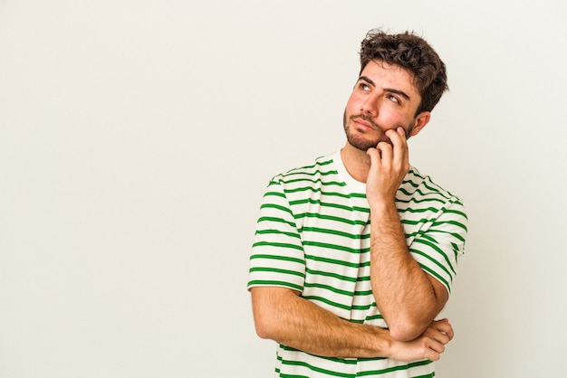 Young caucasian man isolated on white background relaxed thinking about something looking at a copy space.