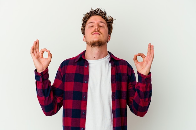 Foto il giovane uomo caucasico isolato su sfondo bianco si rilassa dopo una dura giornata di lavoro, sta eseguendo yoga.