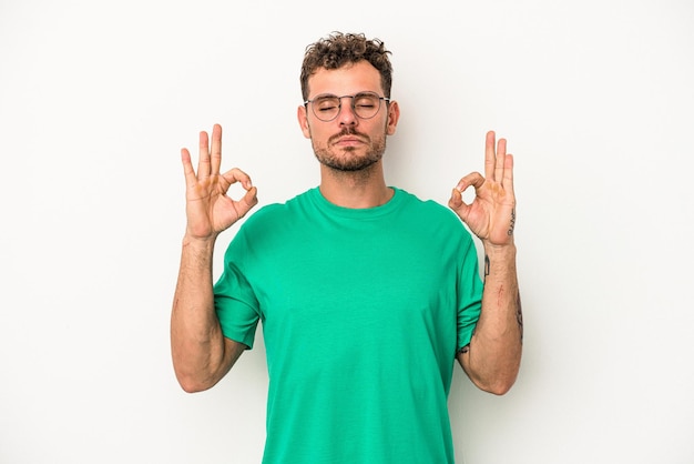 Il giovane uomo caucasico isolato su sfondo bianco si rilassa dopo una dura giornata di lavoro, sta eseguendo yoga.