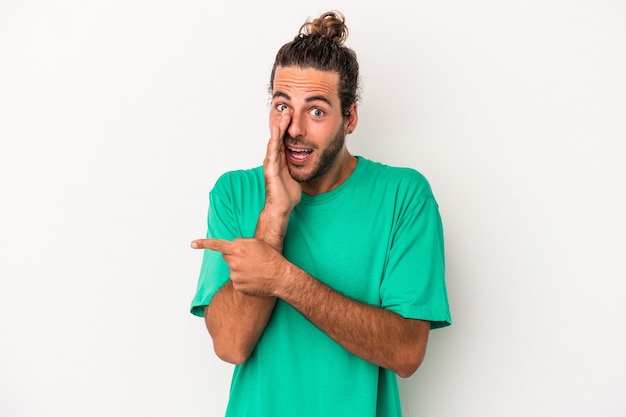 Young caucasian man isolated on white background saying a gossip, pointing to side reporting something.