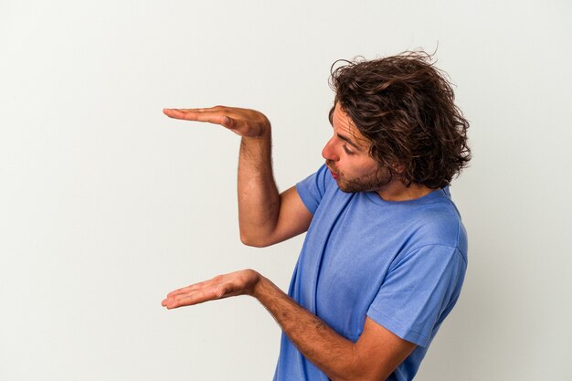 Photo young caucasian man isolated on white background shocked and amazed holding a copy space between hands.