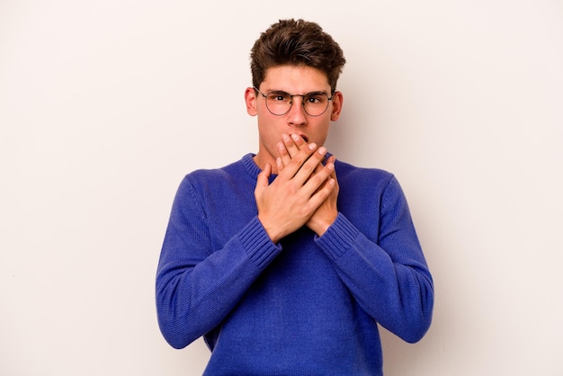 Young caucasian man isolated on white background shocked covering mouth with hands anxious to discover something new