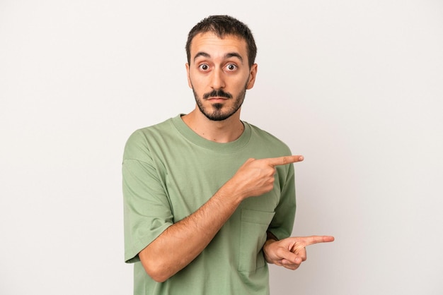 Young caucasian man isolated on white background shocked pointing with index fingers to a copy space