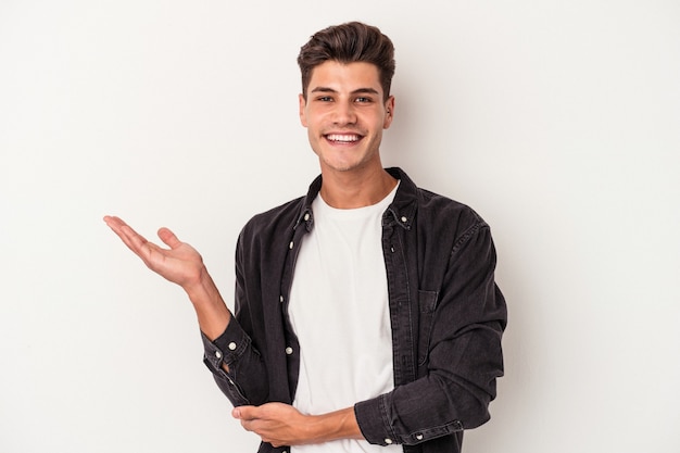 Young caucasian man isolated on white background showing a copy space on a palm and holding another hand on waist.