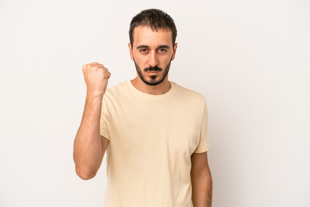 Young caucasian man isolated on white background showing fist to camera, aggressive facial expression.