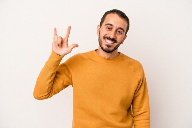 Young caucasian man isolated on white background showing a horns gesture as a revolution concept.