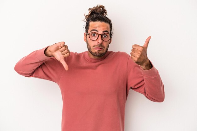 Foto giovane uomo caucasico isolato su sfondo bianco che mostra pollice in alto e pollice in basso, difficile scegliere concept